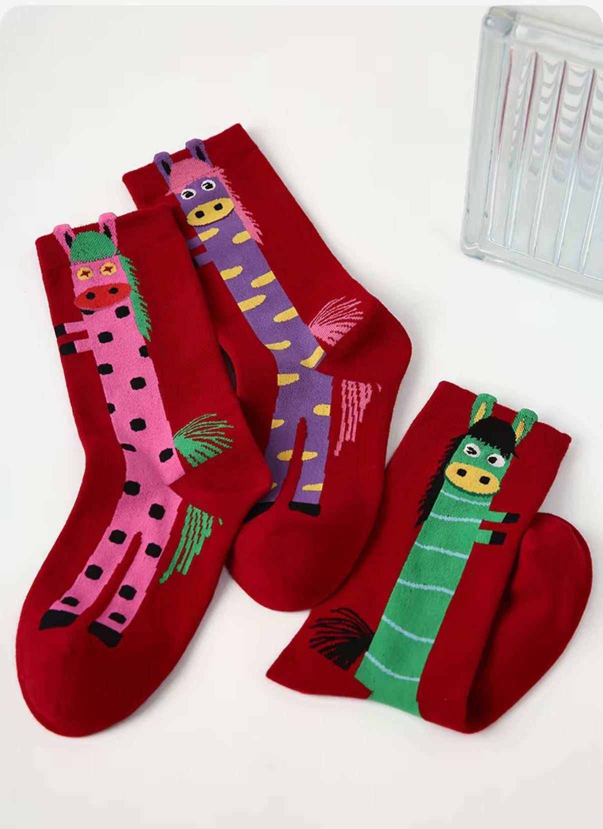Year of Horse socks pack featuring three red socks with playful horse designs in purple, green, and pink